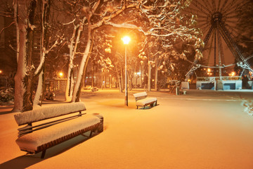 View of bench against christmas tree and shining lantern through snowing.