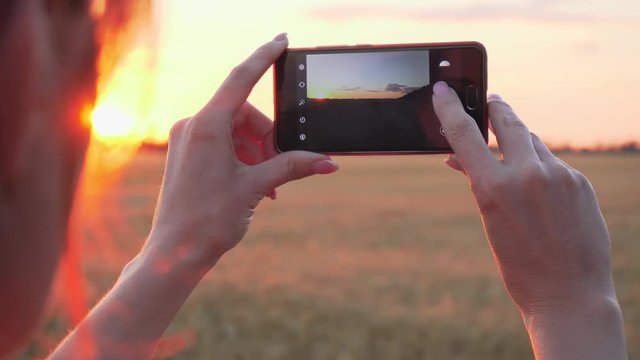 Close up of young woman taking photo of sunset on mobile phone for social networks