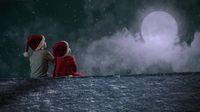 Christmas footage. Cute baby and little kid with Christmas costumes sitting on the roof and waiting for Santa Claus. Winter moonlight night ambient with Santa's sleight silhouette on the moon.