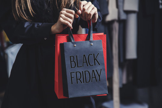 Woman wears black coat holding black friday bag before shop clothes background, sale concept