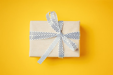 Close up gift box with white ribbon on a yellow background, top view