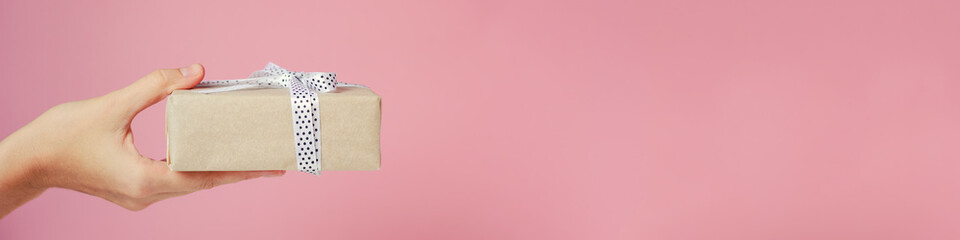 Woman's hand holds gift box on pink background, banner with copy space