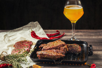 grilled meat steaks on frying pan and glass of beer on a dark wooden background