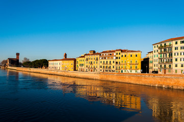 Fototapeta na wymiar Beautiful morning on the river in Pisa, with small houses and blue sky