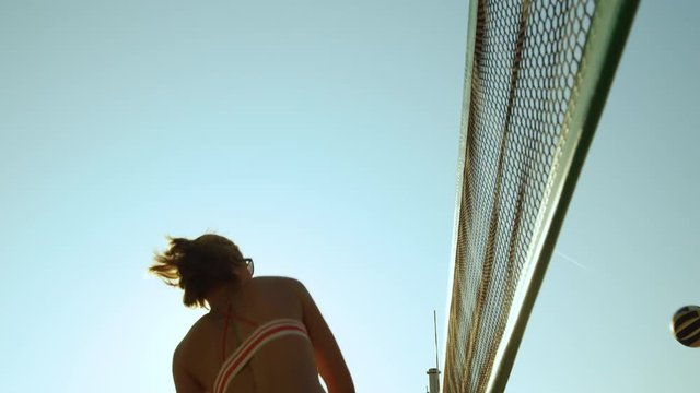 SLOW MOTION, LENS FLARE, CLOSE UP, LOW ANGLE: Young Female Volleyball Player Strikes The Ball Over The Net On A Sunny Day. Cinematic Shot Of Athletic Caucasian Woman Playing Beach Volleyball In Summer