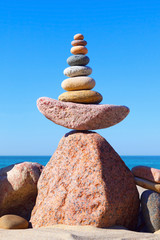 Fototapeta na wymiar High pyramid of multicolored pebbles on a background of the summer sea.