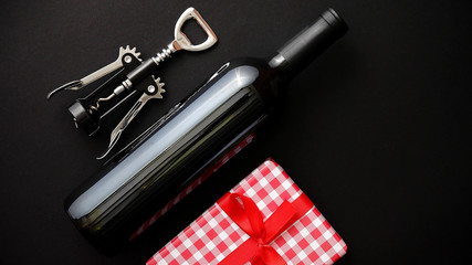 Red wine bottle, corkscrew and boxed christmas gift on black matte background. Top view with copy space