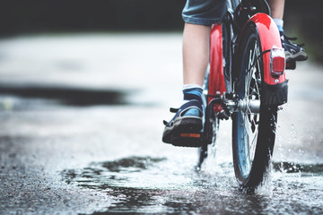 child on a bicycle at asphalt road in summer. Bike in the park moving through puddle on rainy day