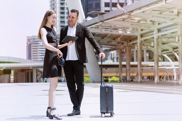 Business couple in black suit standing together with baggage and tablet to talk together happily at out of office before go to aboard.