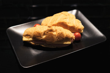 croissant with ham and cheese. Black plate, black background