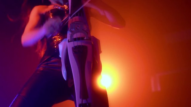 Cellist with electronic cello performs on stage.
