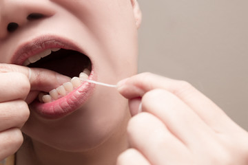 Asian woman using dental floss to remove food and dental plaque from between teeth in areas a...