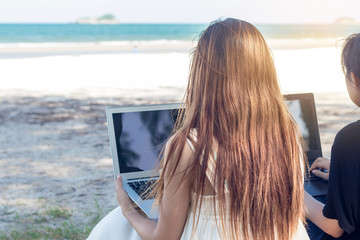 Young Asian woman using laptop in dress sitting on the beach,Girl Freelancer working on sea background