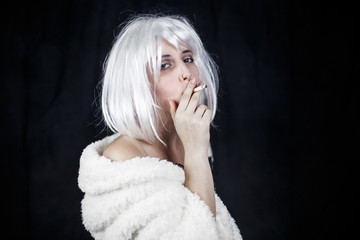 Attractive young woman in costume smoking cigar and looking at camera while standing on black background 