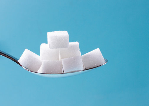 Sugar cubes in spoon on blue background