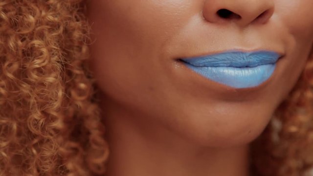 closeup of black womans mouth with bright blue lipstick smiling and showing language
