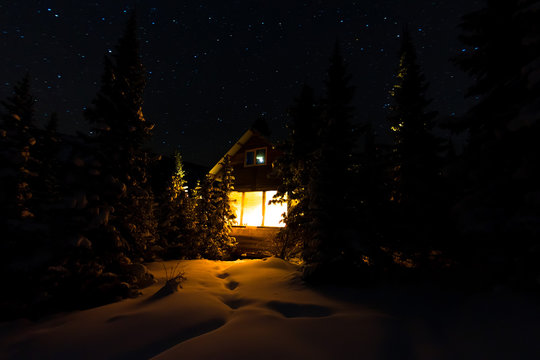 Light from the window of a forest hut under the night sky of the milky way in the winter forest