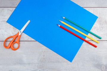 Colorful pencils and sheets of paper on white wooden desk and dark blue background