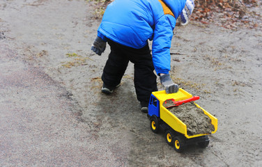 A child in a blue jacket, boots, gloves, hat and black pants playing with a toy plastic machine.