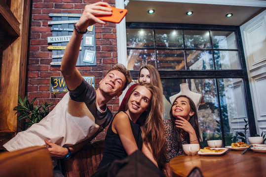 Excited Friends Taking Selfie With Smartphone Sitting At Table Having Night Out.