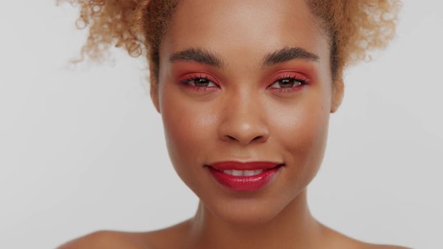 closeup mixed race black womans face with ideal skin and red eyeshadows and red lips smiling