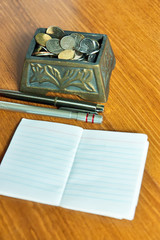 Malaysia ringgit coins inside decorative box, pen and white paper on wood table background.