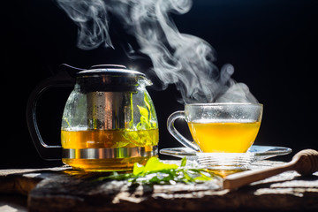 Hot tea in glass cup with steam and lemon .tea leaves and mint herb on wood background