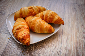 Delicious croissants on a square white plate on a wooden tabletop.
