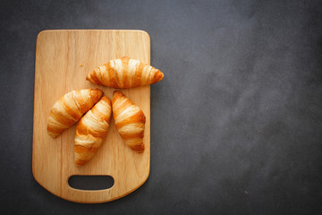 Four croissants on a wooden light cutting board on dark craft paper.