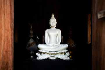 white buddha statue in thai lanna temple with soft-focus and over light in the background