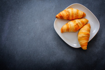 delicious croissants on a dessert white plate on dark craft paper.