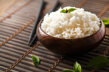 Cooked white rice (Thai Jasmine rice), rice in dark wooden bowl with chopsticks on the wood black bamboo background.