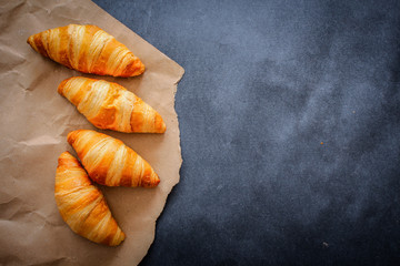 Four croissants on brown craft paper on a dark contrasting background.