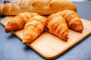 French loaf and four croissants on a wooden cutting board on dark craft paper.