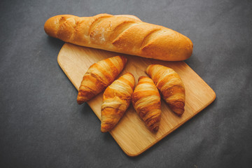 French loaf and four croissants on a wooden cutting board on dark craft paper.