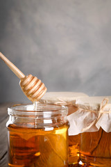 Pouring aromatic honey into jar, closeup. Honey in glass jars and honeycombs wax on wooden...
