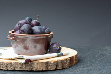 Violet, large, ripe plums on a wooden stand, on a black background