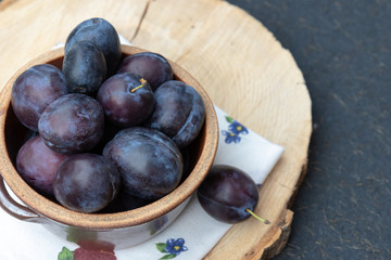 Violet, large, ripe plums on a wooden stand, on a black background