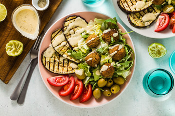 an appetizing dinner or lunch from a salad with tomatoes, grilled eggplants and legume falafel with sesame tahini dressing. Vegan healthy food for the whole family