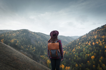 Young girl with backpack and hat view back on the background of autumn nature