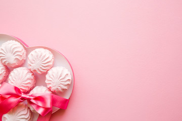 Fluffy, airy zephyrs in box of heart shape with ribbon for beloved. Mockup for different ideas. Empty place for positive, sentimental text, lovely quote or sayings on pastel pink table. Top view.
