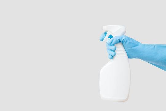 Cleaner's hand in blue rubber protective glove holding a white chemical spray bottle. Empty place for text or logo on gray background. Early spring or regular cleanup. Commercial cleaning company.