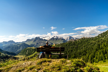 Wunderschöner Ausblick auf die  Berge in den den Alpen mit einer Person auf einer Bank im Vordergrund