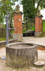 Brunnen mit Wasserpumpe vor altem Eisentor