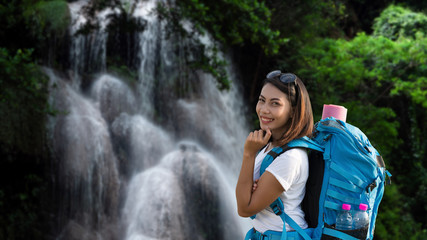 Beautiful happy and smiling tourist woman having fun with backpack on waterfall background. Lifestyle Travel concept.