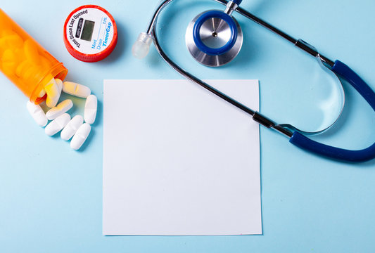 White pills in orange bottle with stethoscope on blue background, copy space on white paper note