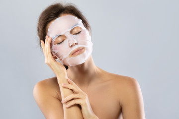 Woman with a sheet moisturizing mask on her face isolated on gray background
