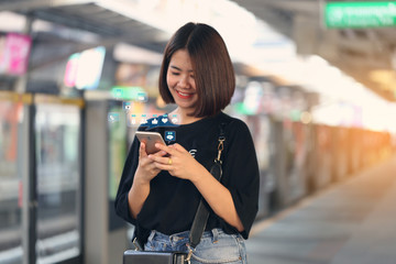 Happy hipster girl hand holding smartphone with hologram or icon of set of social media on BTS sky train in bangkok background, Communication technology and Social media concept