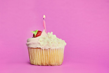 Pretty strawberry or cherry flavored frosted cupcake decorated with white chocolate shavings and one candle burning. Free space for copy text.