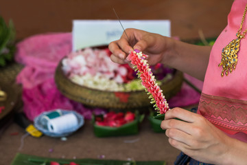 A asian woman stringing Thai tranditional jasmine garlands decorated with colorful flower petals